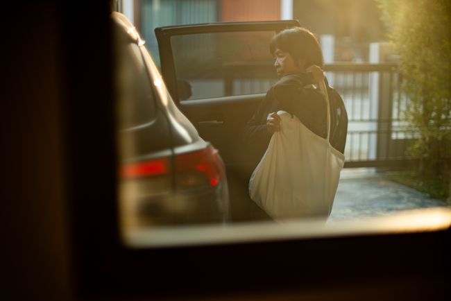 Woman next to a car with the door open, seen through a window
