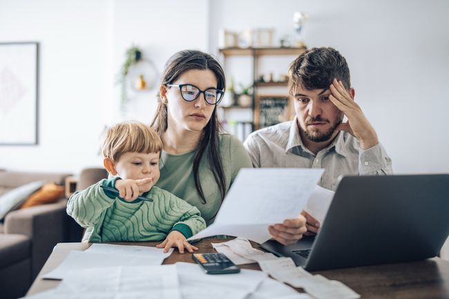 A couple with a young child sitting in front of a laptop examining their bills and looking stressed